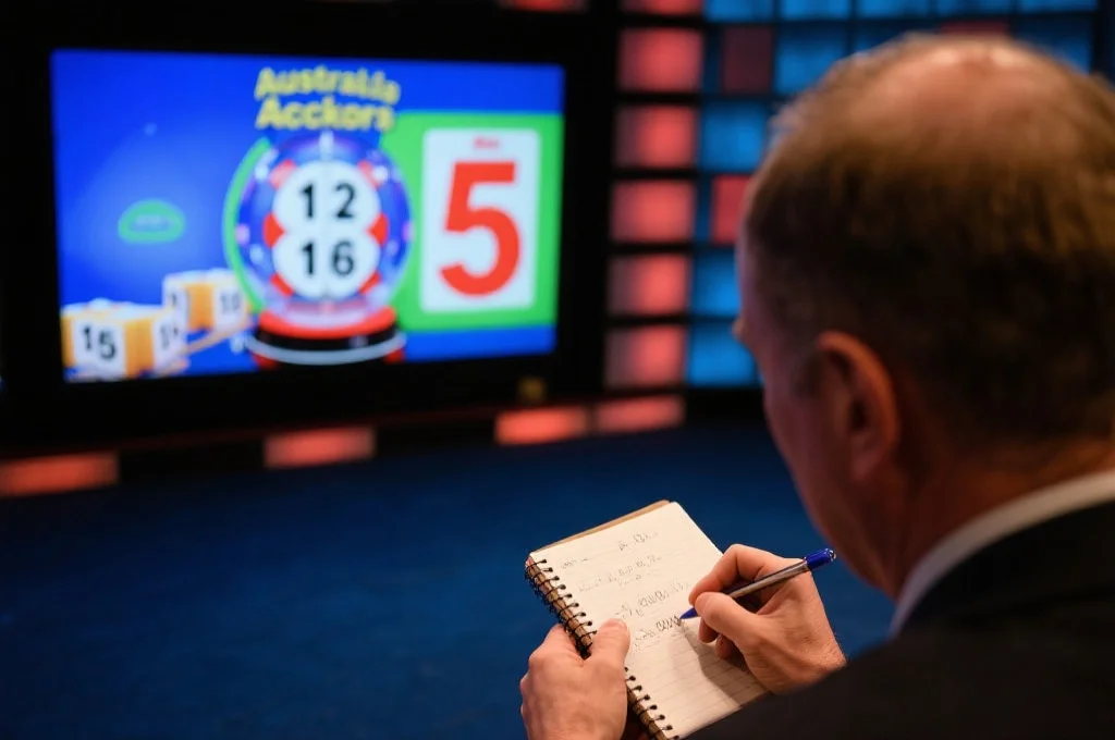 一位观众正在笔记本上记录开奖直播的开奖号码,屏幕上显示澳洲幸运5抽奖过程